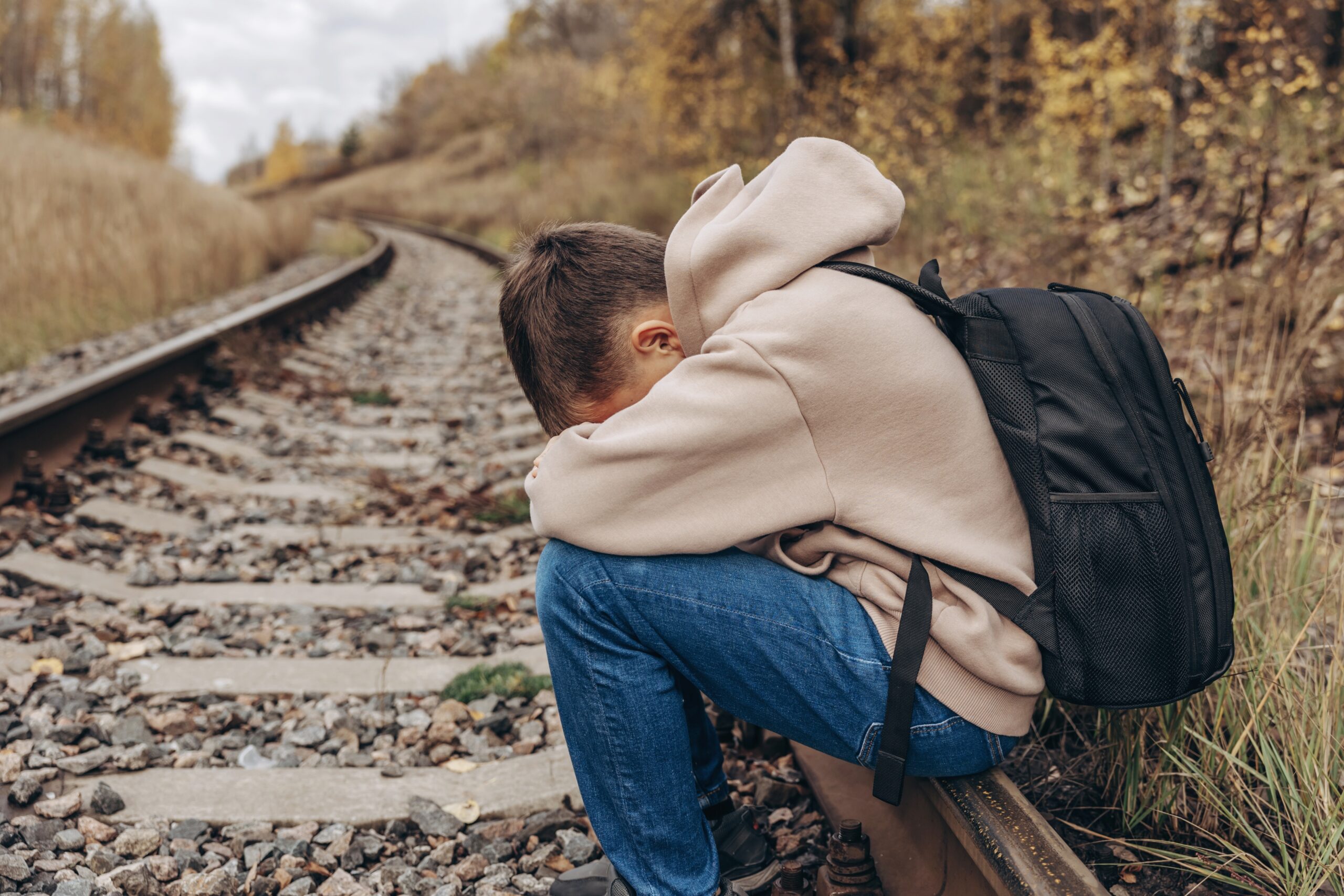 Sad,Teenager,Boy,With,Backpack,Sitting,On,Rails,Of,Railway.